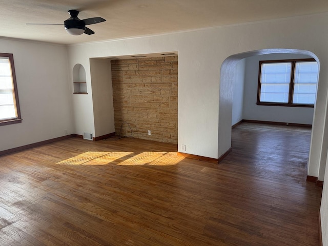 unfurnished room with arched walkways, wood finished floors, and a ceiling fan