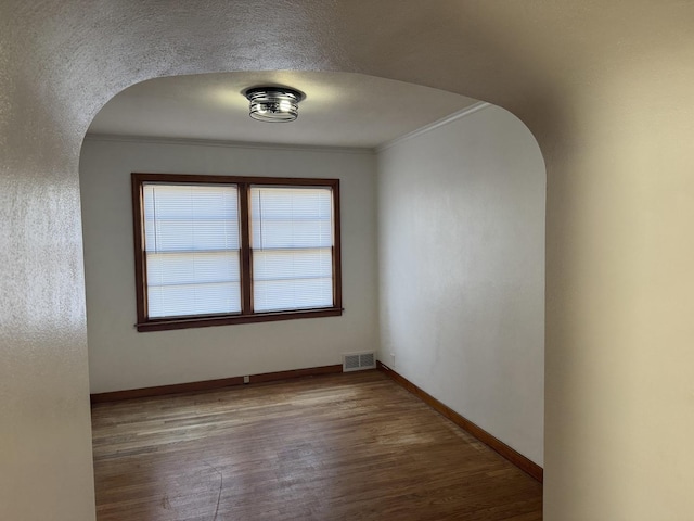 unfurnished room with arched walkways, visible vents, ornamental molding, and wood finished floors