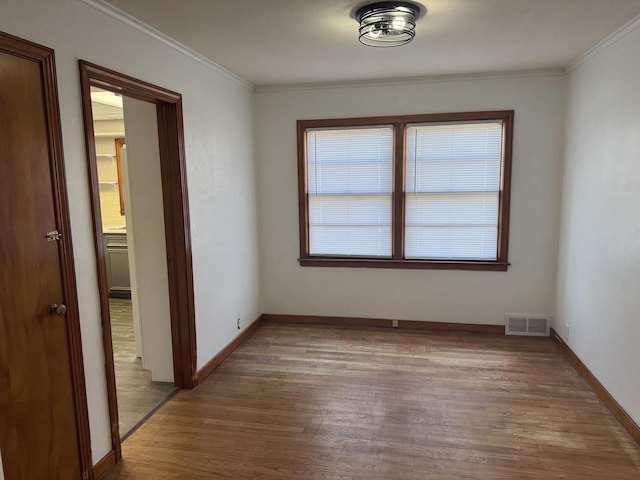 empty room featuring visible vents, baseboards, wood finished floors, and crown molding