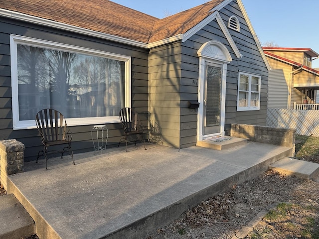 entrance to property featuring fence and a shingled roof