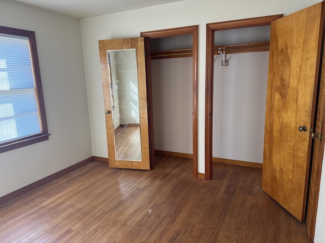 unfurnished bedroom with multiple closets, baseboards, and wood finished floors