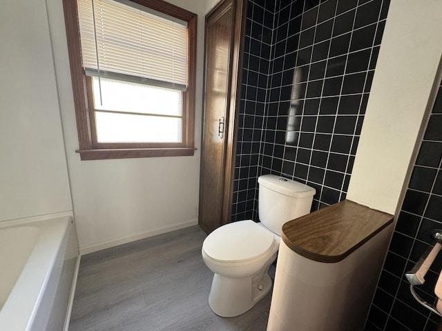 bathroom with tile walls, toilet, wood finished floors, and a shower