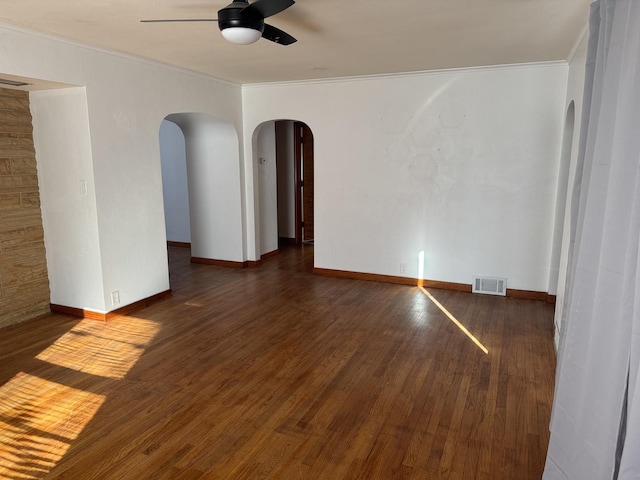 spare room with visible vents, ornamental molding, dark wood finished floors, arched walkways, and ceiling fan