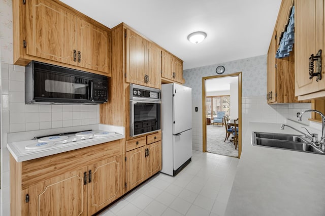 kitchen with white appliances, wallpapered walls, a sink, light countertops, and tasteful backsplash