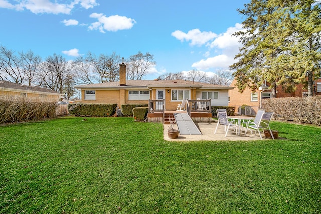 back of house with a patio, a chimney, a deck, a lawn, and brick siding