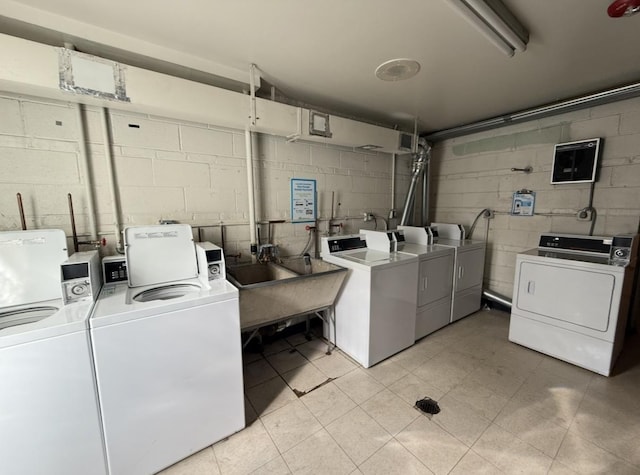 shared laundry area featuring concrete block wall, washing machine and dryer, and a sink