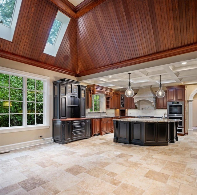 kitchen featuring coffered ceiling, a skylight, a kitchen island with sink, a sink, and custom range hood