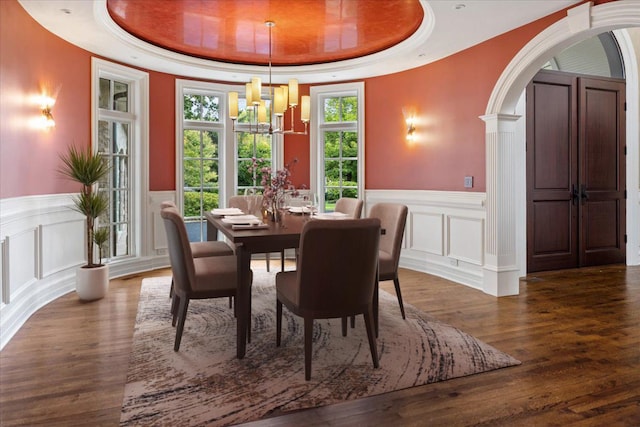 dining area featuring a wainscoted wall, a tray ceiling, wood finished floors, arched walkways, and a chandelier