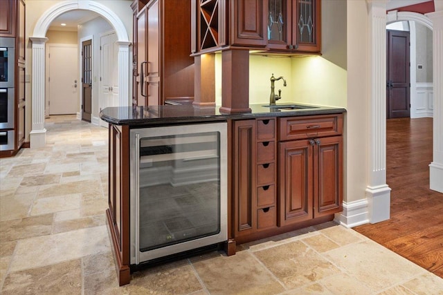 bar featuring beverage cooler, arched walkways, a sink, indoor wet bar, and stone finish flooring