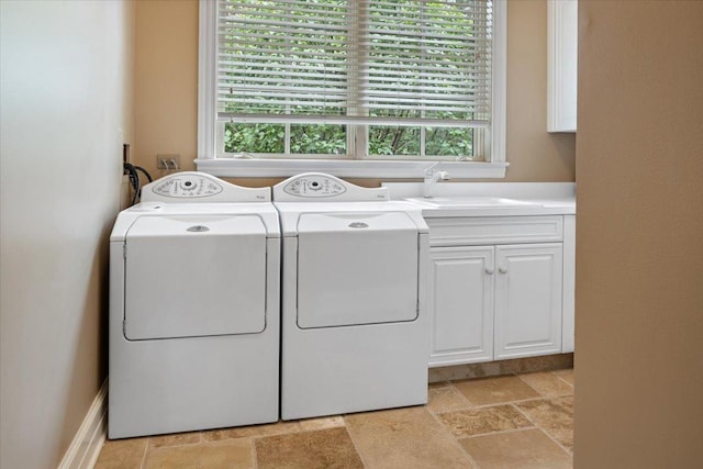 laundry area with cabinet space, separate washer and dryer, stone tile flooring, and a sink