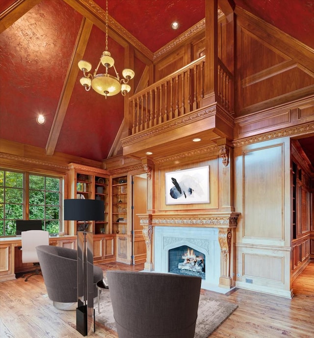 living room featuring a notable chandelier, high vaulted ceiling, built in features, a decorative wall, and light wood finished floors