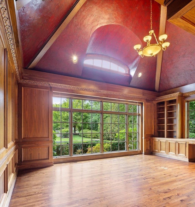 unfurnished living room featuring an inviting chandelier, a decorative wall, wood finished floors, and high vaulted ceiling