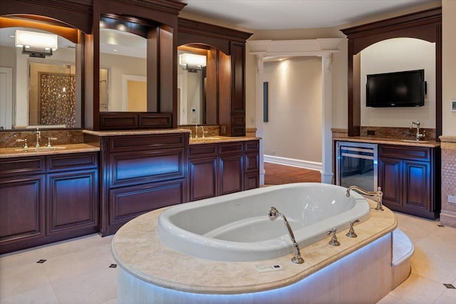 bathroom featuring beverage cooler, double vanity, a tub to relax in, and a sink