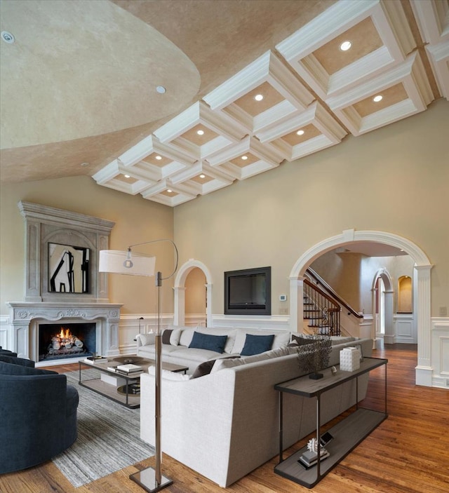 living area with coffered ceiling, beam ceiling, arched walkways, a lit fireplace, and a towering ceiling