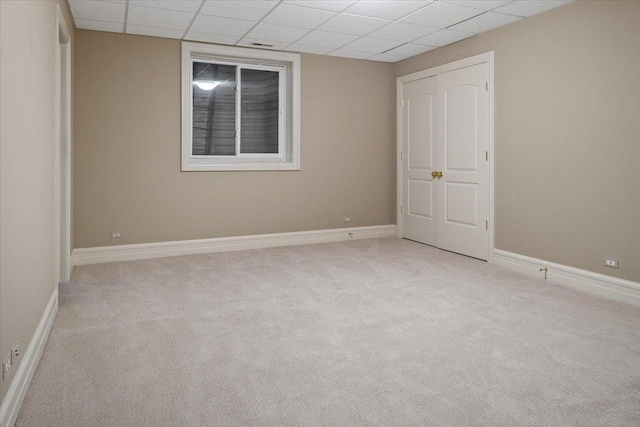 carpeted empty room featuring baseboards and a drop ceiling