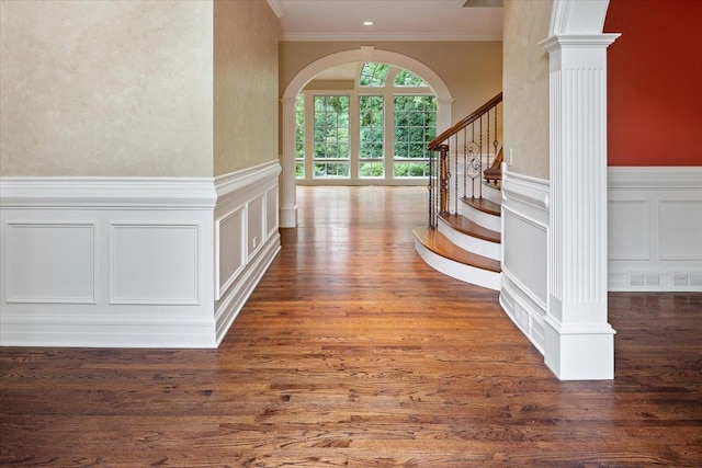 corridor featuring wood finished floors, visible vents, decorative columns, arched walkways, and crown molding