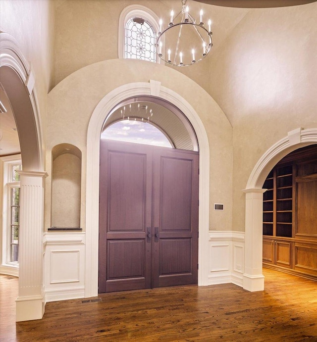 entrance foyer featuring wood finished floors, a high ceiling, wainscoting, a decorative wall, and a notable chandelier