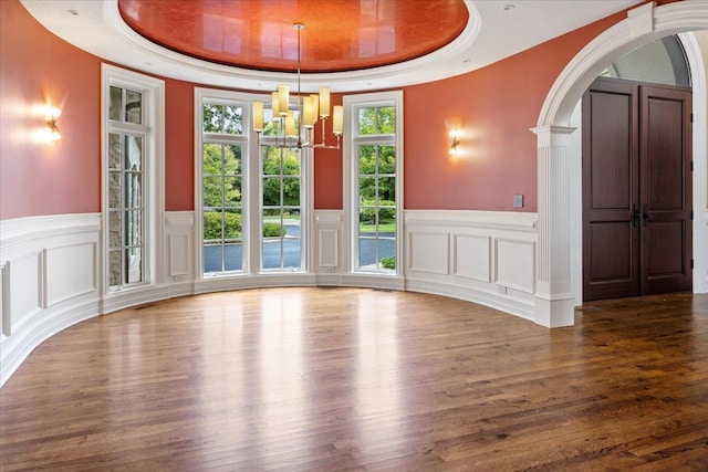 interior space with arched walkways, an inviting chandelier, a tray ceiling, and wood finished floors