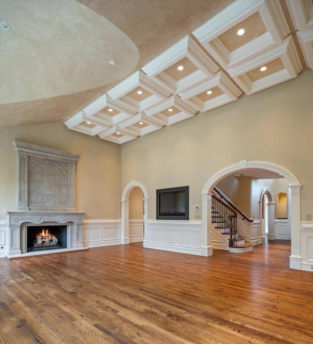 unfurnished living room with wood finished floors, beam ceiling, arched walkways, a lit fireplace, and stairs