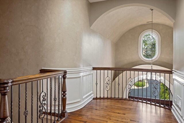 staircase featuring vaulted ceiling, wainscoting, an inviting chandelier, hardwood / wood-style flooring, and arched walkways