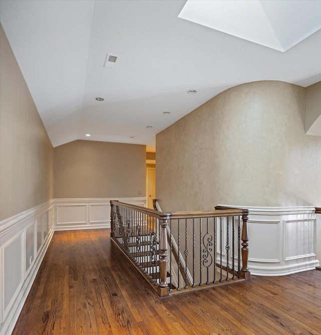 hallway with an upstairs landing, wood finished floors, and lofted ceiling with skylight