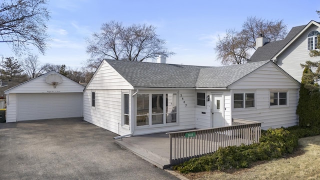 view of front facade with an outbuilding, a shingled roof, a detached garage, and a deck