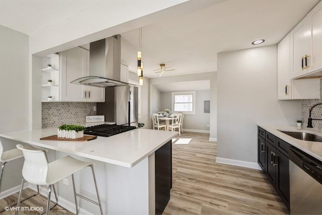 kitchen with a sink, stainless steel appliances, light countertops, and wall chimney range hood