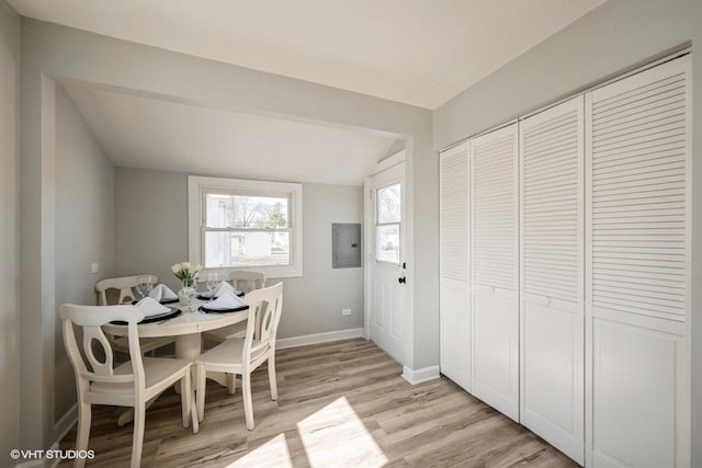 dining area with electric panel, light wood-type flooring, lofted ceiling, and baseboards