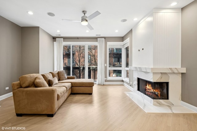 living room featuring light wood-style flooring, a fireplace, baseboards, and ceiling fan