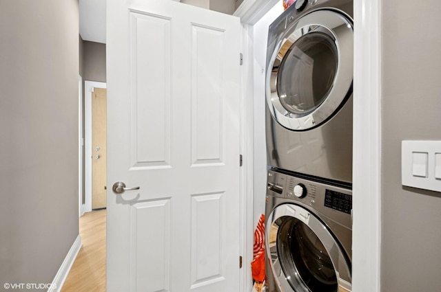 clothes washing area featuring laundry area, light wood-style floors, stacked washer and clothes dryer, and baseboards