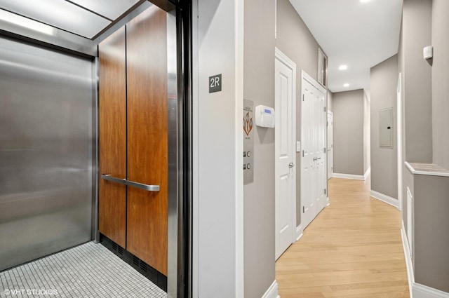 hallway featuring elevator, recessed lighting, baseboards, and light wood finished floors