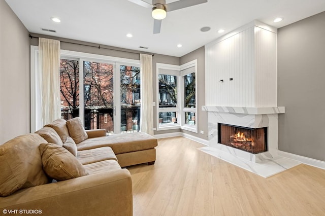 living area featuring visible vents, wood finished floors, a fireplace, baseboards, and ceiling fan