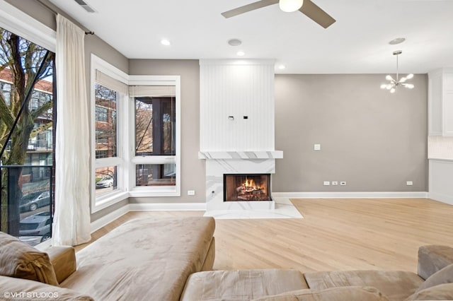 living area featuring light wood finished floors, a large fireplace, baseboards, recessed lighting, and ceiling fan with notable chandelier