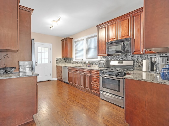 kitchen featuring light stone countertops, dark wood finished floors, a sink, decorative backsplash, and stainless steel appliances