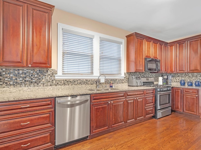 kitchen featuring light stone counters, a sink, decorative backsplash, light wood-style floors, and appliances with stainless steel finishes