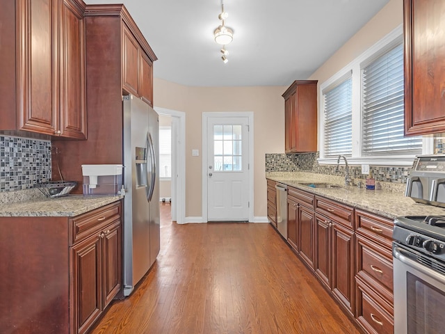 kitchen with light stone counters, a sink, dark wood finished floors, appliances with stainless steel finishes, and decorative backsplash