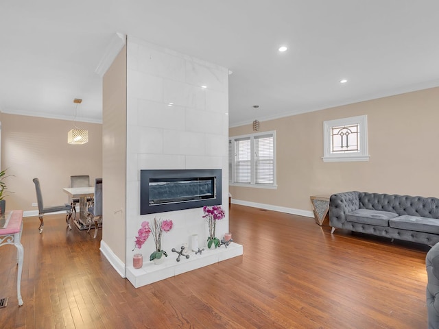 living room with baseboards, a tiled fireplace, ornamental molding, recessed lighting, and wood finished floors