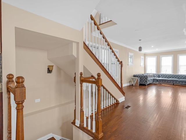 staircase with visible vents, crown molding, baseboards, and wood finished floors