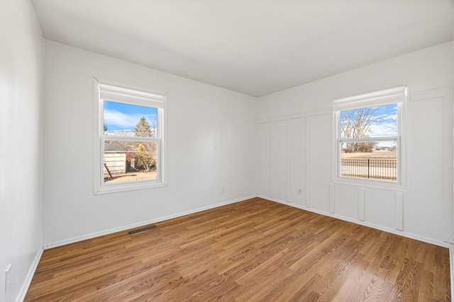 empty room featuring visible vents, baseboards, a healthy amount of sunlight, and wood finished floors