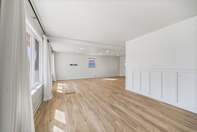 empty room featuring light wood-style flooring, wainscoting, and a decorative wall