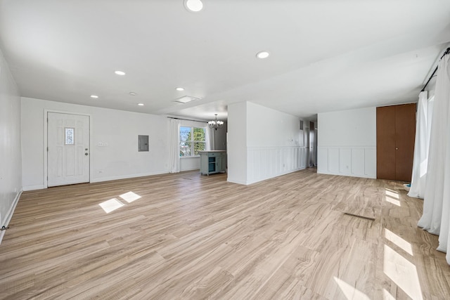 unfurnished living room with a wainscoted wall, electric panel, recessed lighting, light wood-type flooring, and a chandelier