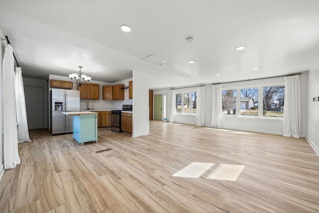 kitchen with stainless steel refrigerator with ice dispenser, range with gas stovetop, open floor plan, a center island, and brown cabinetry