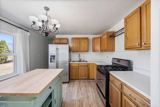 kitchen with a notable chandelier, light wood-style flooring, a sink, stainless steel appliances, and wooden counters