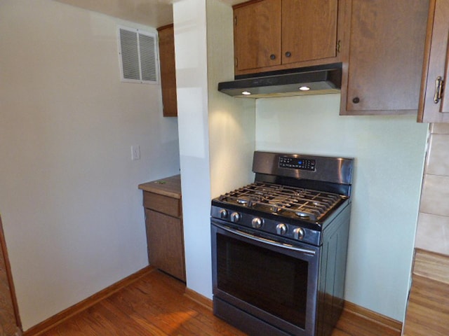 kitchen with visible vents, under cabinet range hood, wood finished floors, baseboards, and gas range