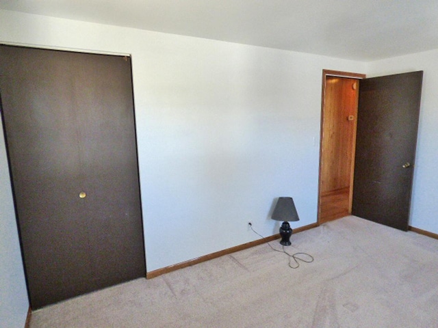 unfurnished bedroom featuring light carpet, a closet, and baseboards