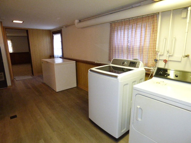 laundry room with laundry area, wooden walls, wood finished floors, and independent washer and dryer