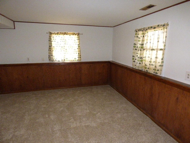 carpeted empty room featuring crown molding, wooden walls, and a wainscoted wall