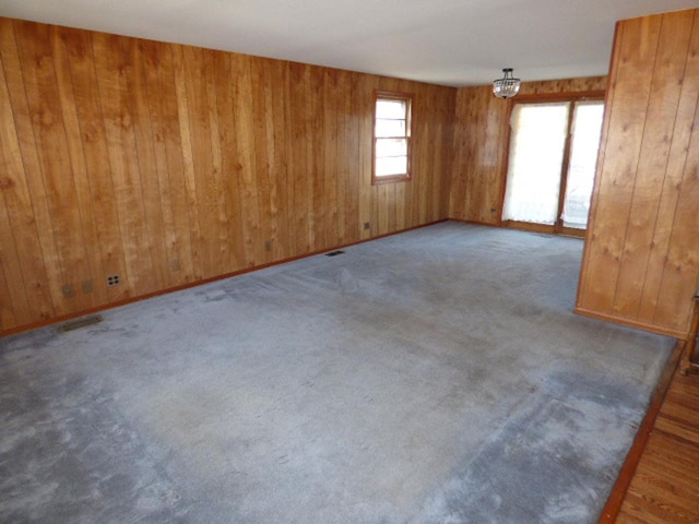 carpeted empty room featuring an inviting chandelier, wooden walls, and baseboards