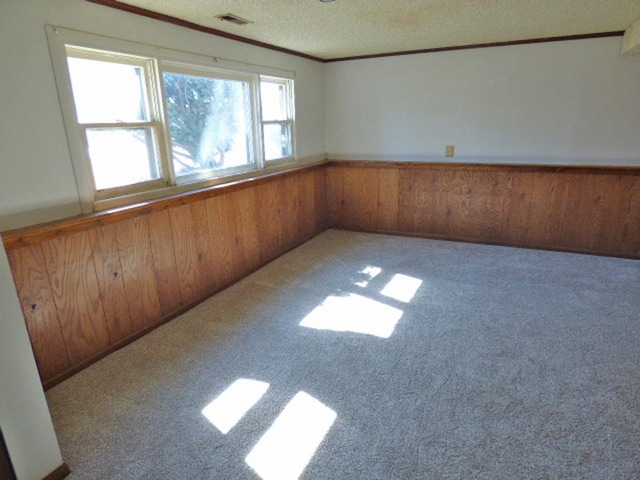 carpeted spare room with visible vents, wainscoting, wood walls, a textured ceiling, and crown molding