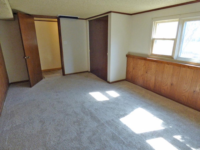 unfurnished bedroom with light colored carpet, multiple closets, a textured ceiling, and crown molding